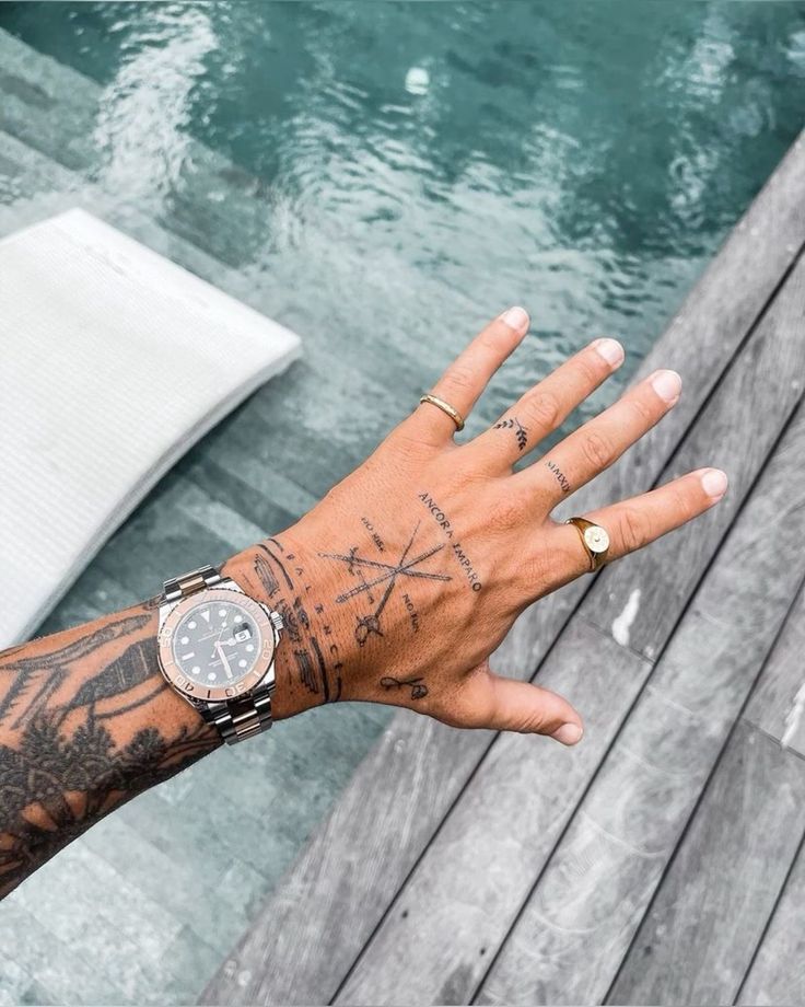 Tattooed hand with a watch and rings beside a pool, showcasing unique designs and casual style.