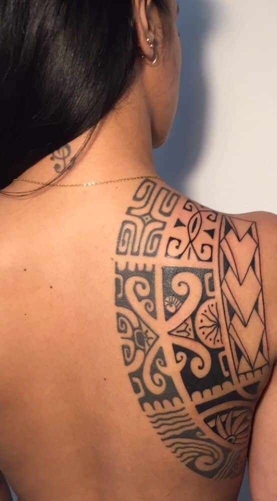 Back view of a woman with intricate Polynesian tattoo patterns on shoulder and upper back.