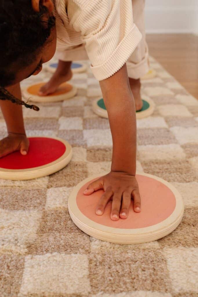 Child playing balance game with colorful wooden stepping stones on a checkered carpet.