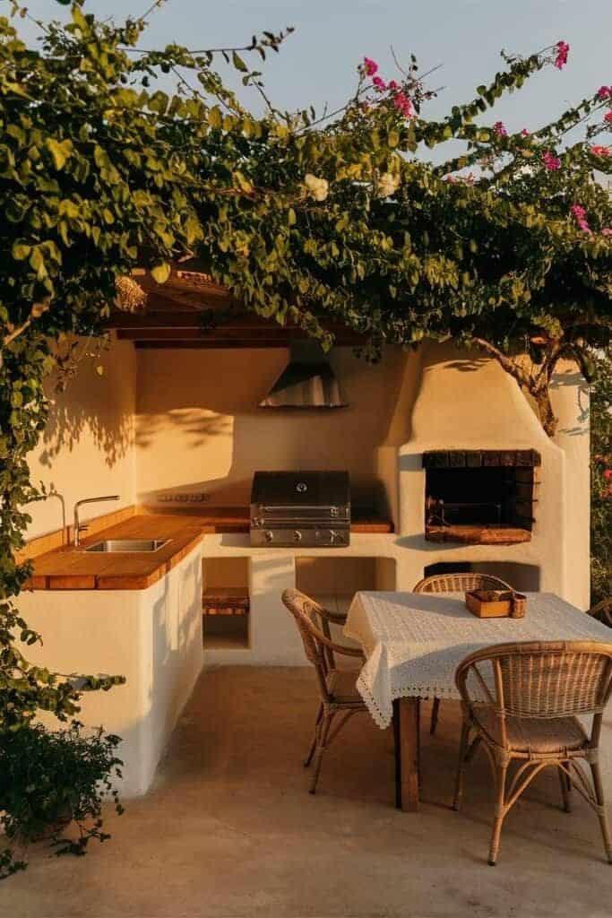 15 Outdoor Kitchen Inspirations_ Create Your Dream Backyard Oasis Outdoor kitchen with BBQ, dining table, and vine-covered pergola, perfect for cozy al fresco gatherings. | Sky Rye Design Outdoor kitchen with BBQ, dining table, and vine-covered pergola, perfect for cozy al fresco gatherings.