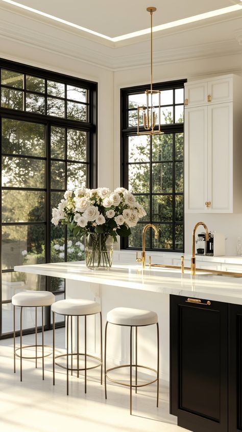 Elegant kitchen with large windows, white cabinets, gold accents, and a vase of white roses on the island countertop.