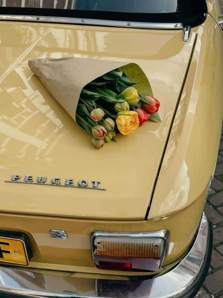 Bouquet of tulips on a vintage yellow Peugeot car trunk, creating a charming retro aesthetic.