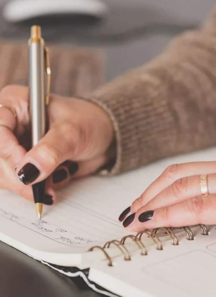 Person writing notes in a spiral notebook with a pen, focusing on hands and pen close-up.