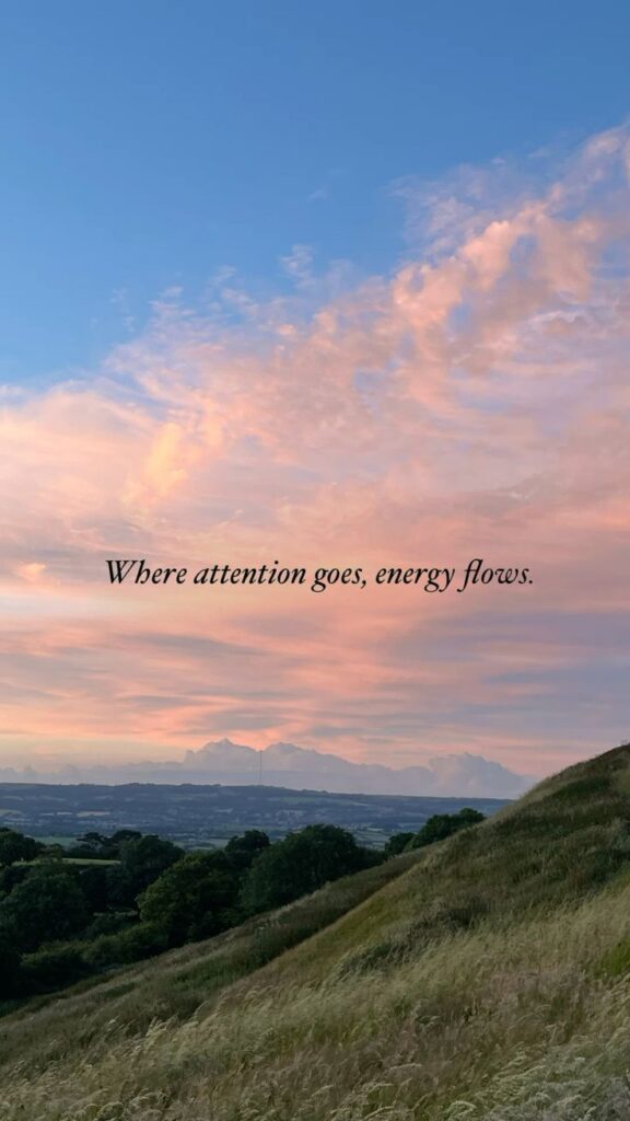 Scenic landscape with pink sunset sky and grassy hills, featuring quote: Where attention goes, energy flows.