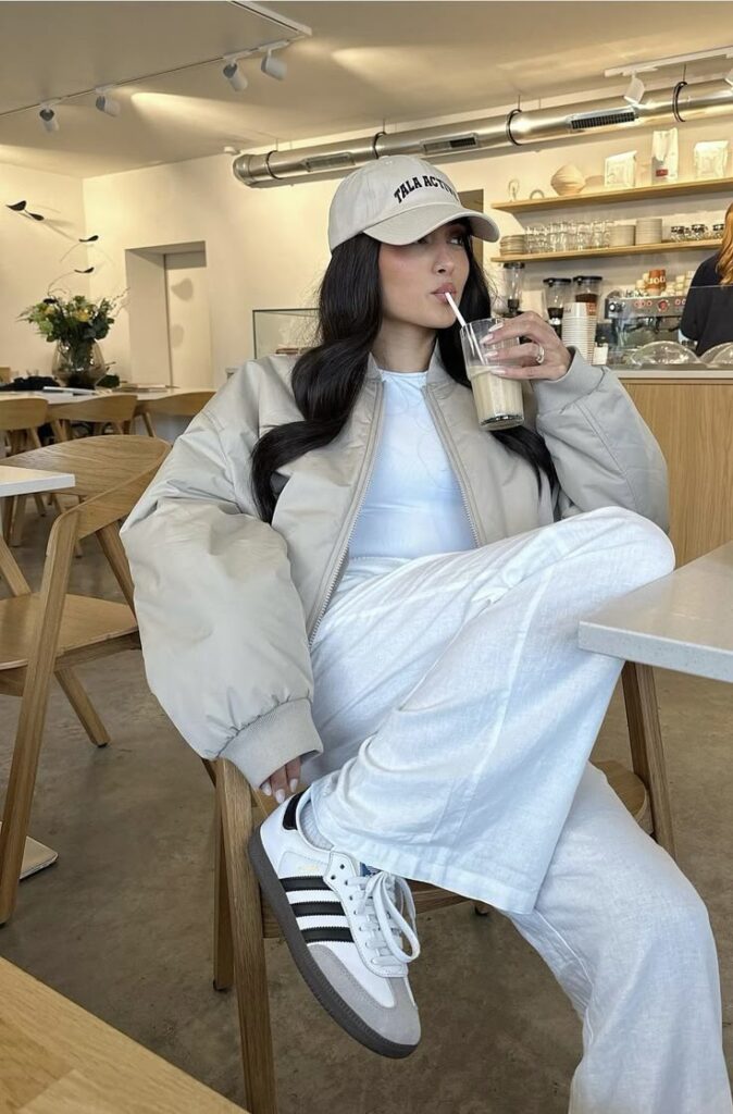 Woman in casual outfit sipping iced coffee at a stylish café, wearing a cap and sneakers.
