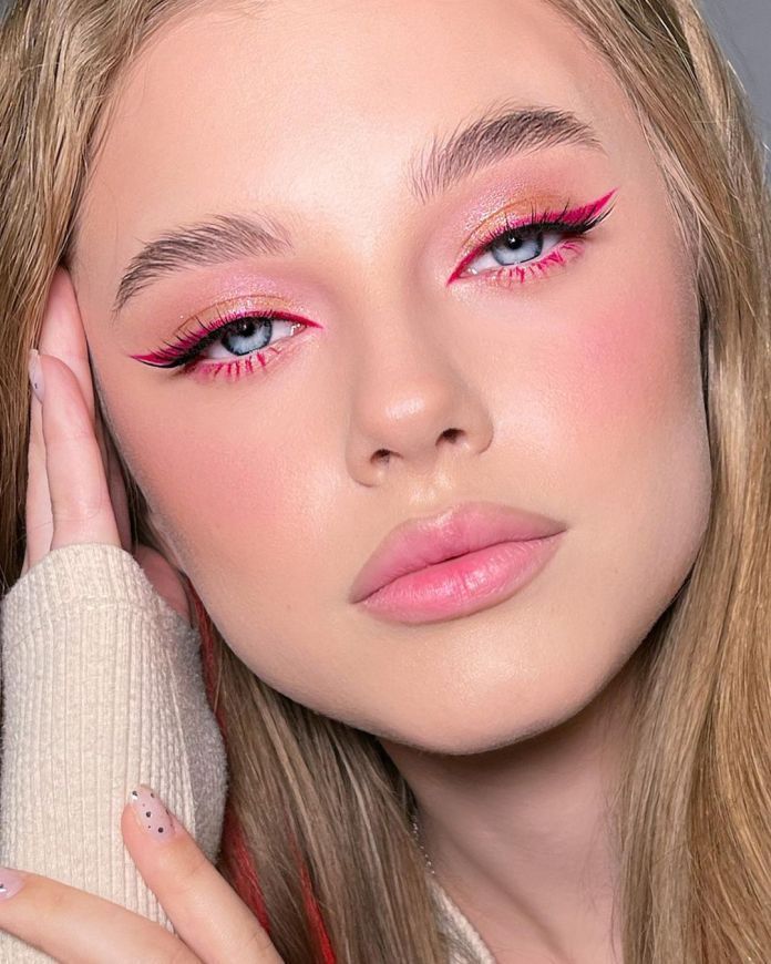 Woman with pink eyeliner, blush, and natural makeup posing with her hand near her face. Elegant beauty look.