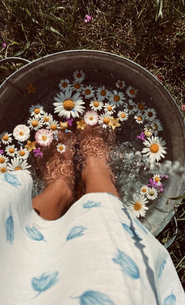 Feet soaking in a daisy-filled metal tub outdoors on a sunny day, relaxation and nature concept.