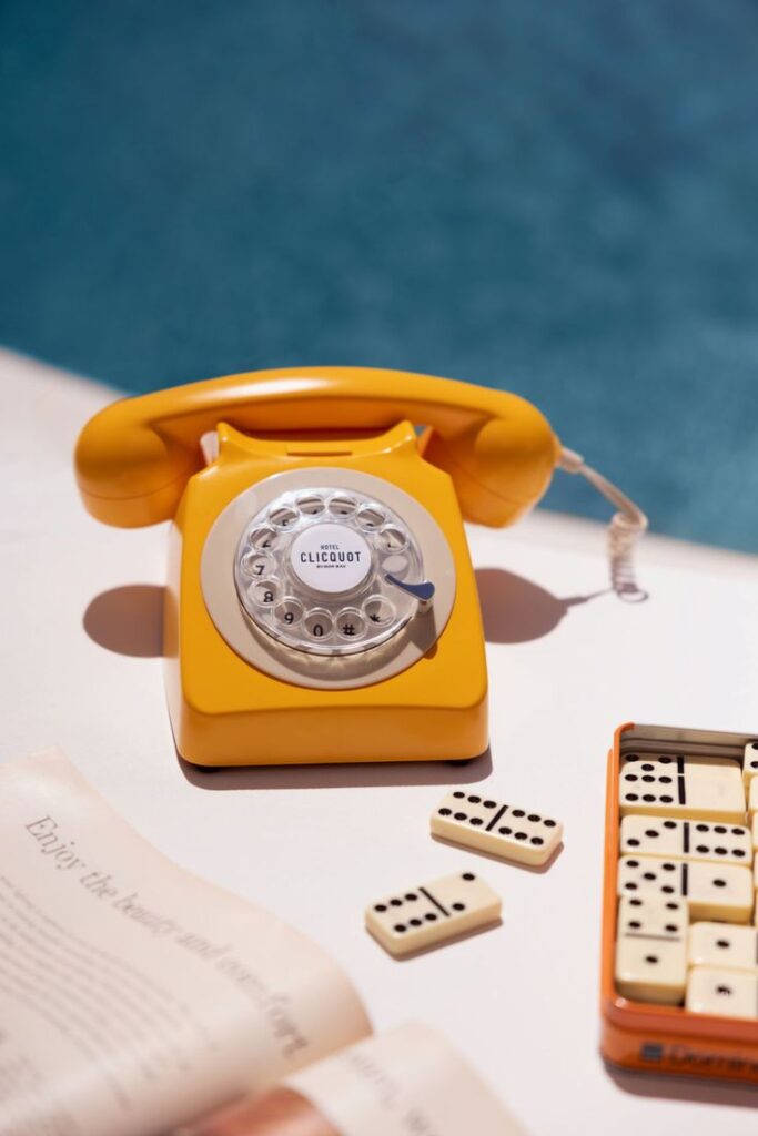 Bright yellow rotary phone and dominoes by a poolside.