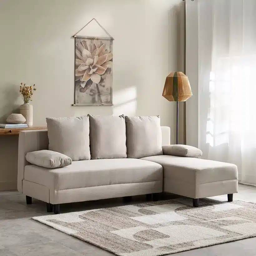 Beige L-shaped sofa in a cozy living room with modern decor and natural light from a window.