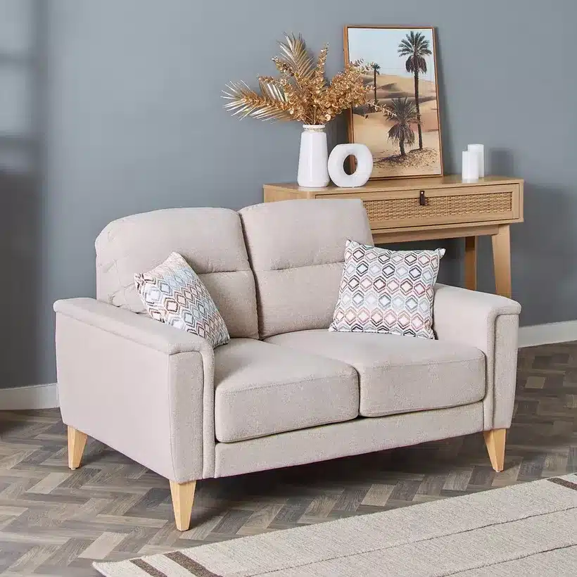 Beige loveseat with patterned cushions, wood legs, and nearby console table with desert-inspired decor.