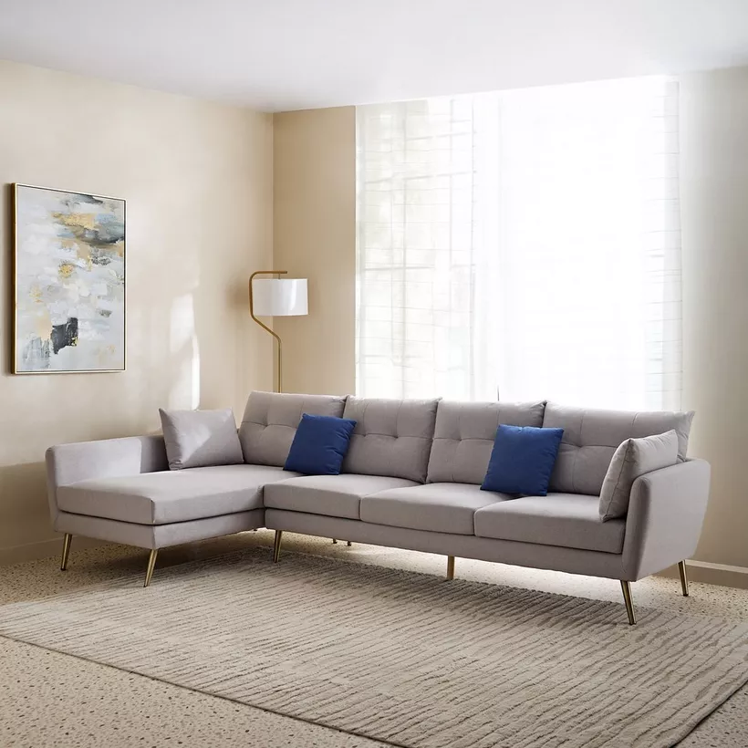 Modern gray sectional sofa with blue pillows in a bright living room, featuring a floor lamp and abstract wall art.