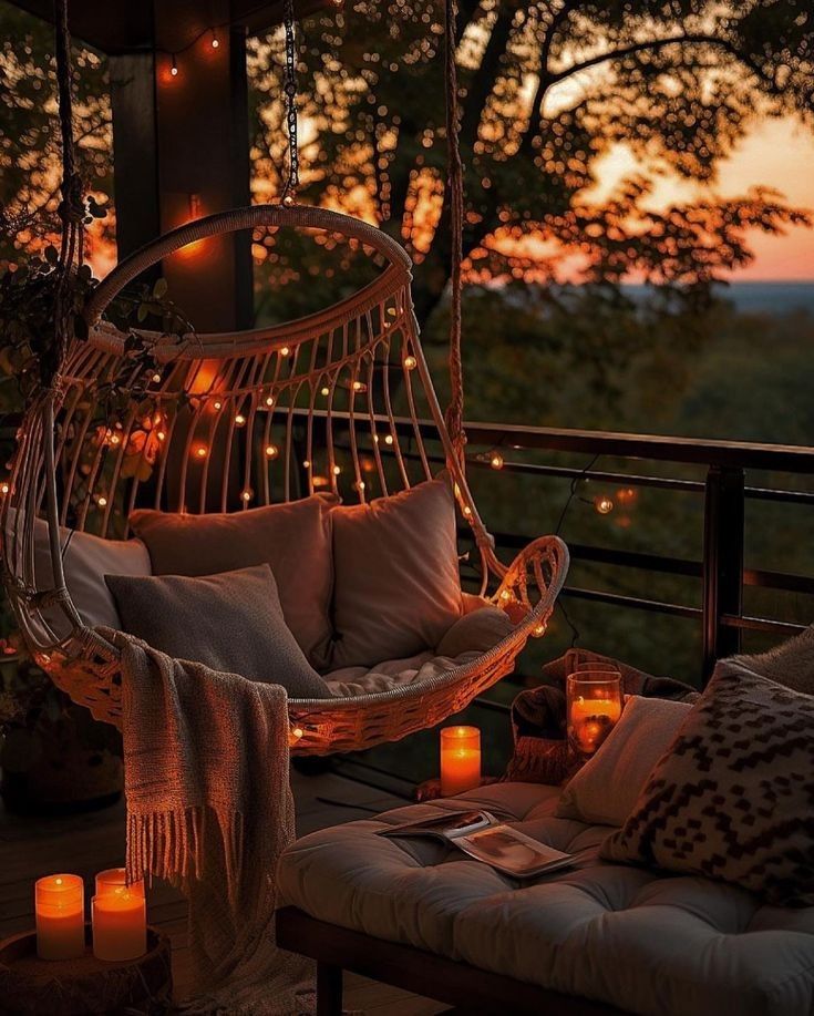 Cozy patio with a hanging chair, pillows, blankets, candles, and string lights at sunset. Perfect for relaxation.