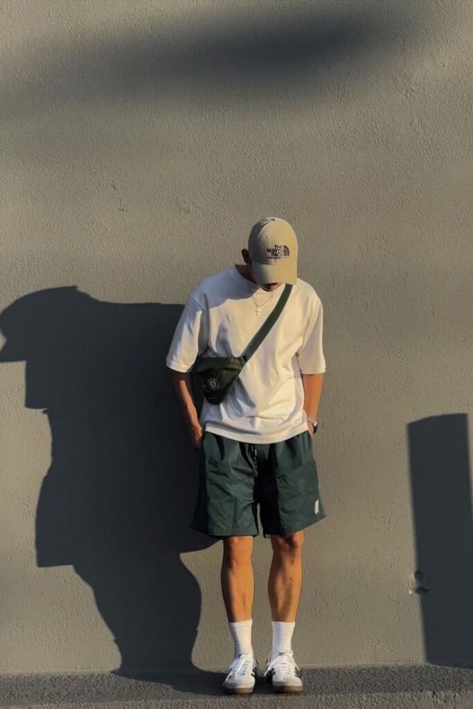 Man in casual outfit with cap and crossbody bag, casting shadow on a wall.