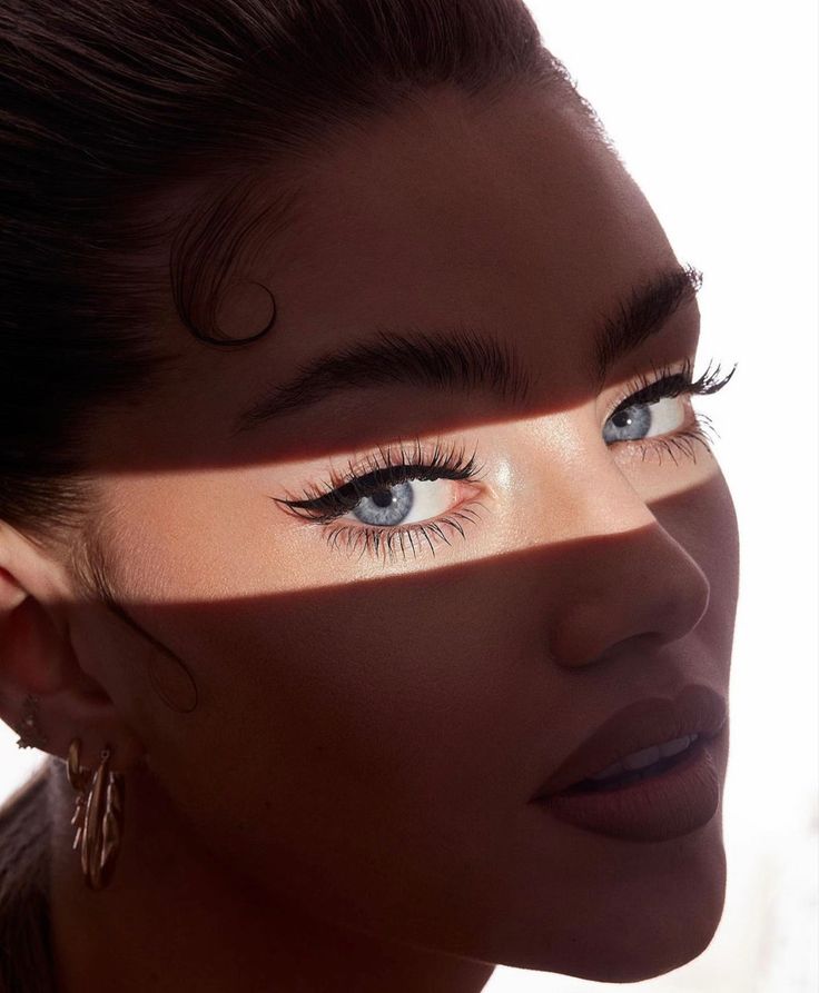 Close-up of a woman's face with dramatic eye makeup, highlighted by sunlight and shadows.