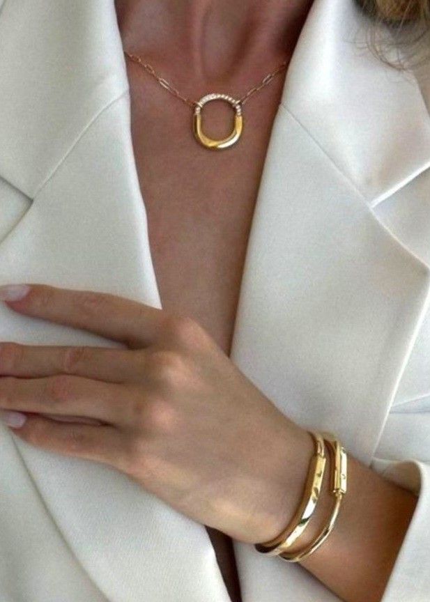 Woman in white blazer wearing a gold necklace and bracelets, showcasing elegant jewelry and fashion style.
