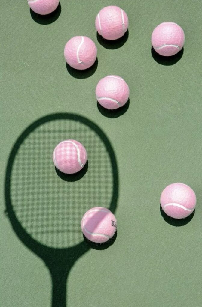 Pink tennis balls and a racket shadow on a green court, creating a vibrant and playful sports scene.