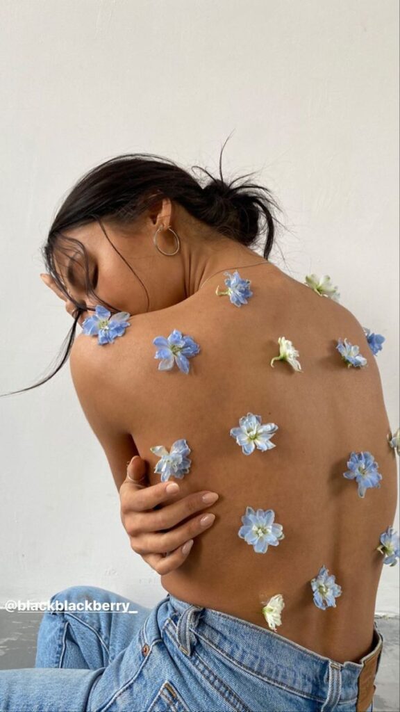 Woman with back adorned in blue flowers and wearing jeans, embracing nature in minimalistic setting.