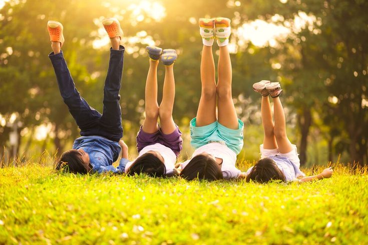 Children lying on grass with feet raised, enjoying a sunny day in the park. Outdoor Games for Kids