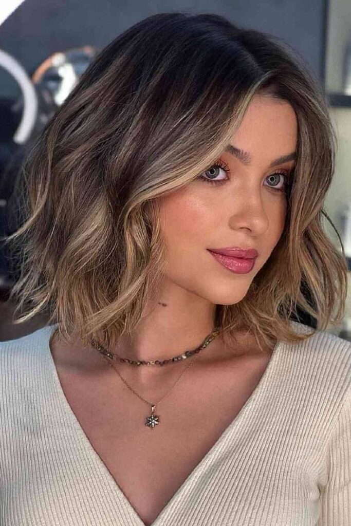Woman with wavy, shoulder-length blonde hair, wearing a cream top and necklace, showcasing a chic hairstyle look.