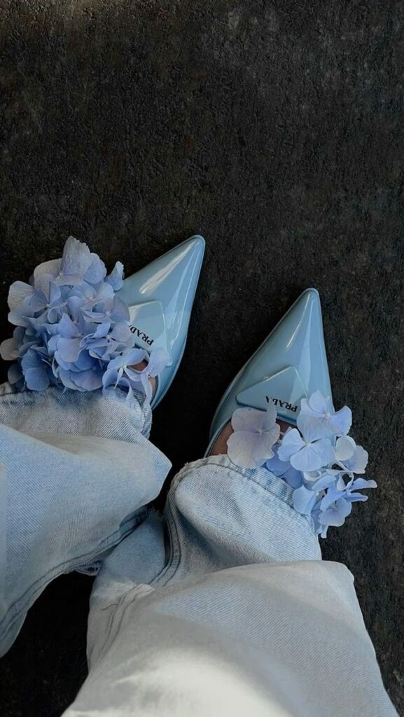 Stylish blue pointed shoes adorned with pastel flowers and denim jeans on dark background.