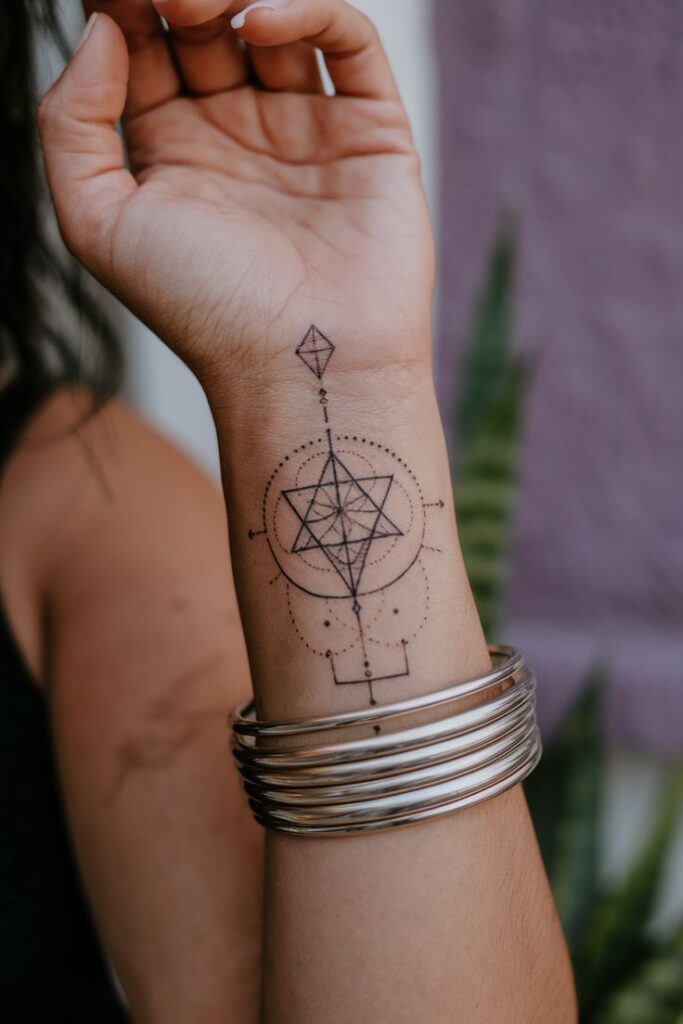 Geometric wrist tattoo with abstract design, silver bangles, close-up on forearm.