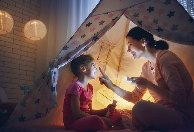 Mother and daughter enjoy bedtime story inside a cozy tent with warm lighting.