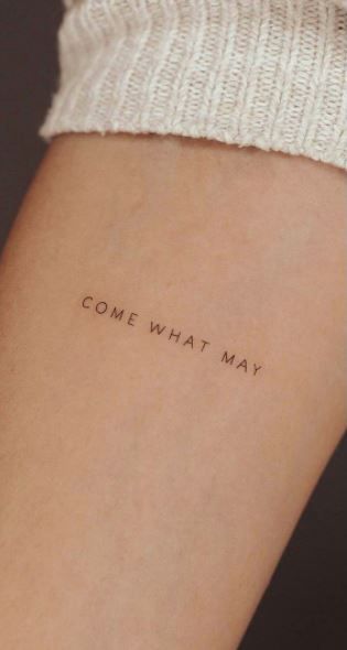 Tattoo reading COME WHAT MAY on forearm, symbolizing resilience and acceptance.