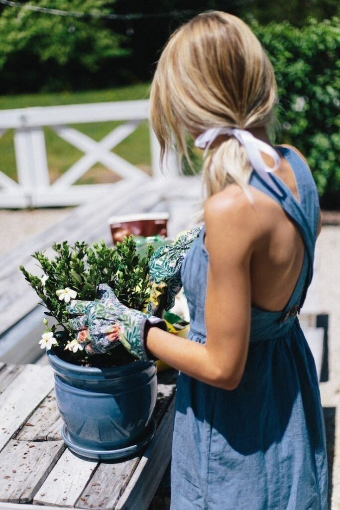 Gardener in blue dress tending plants in a pot outdoors, summer gardening scene.
