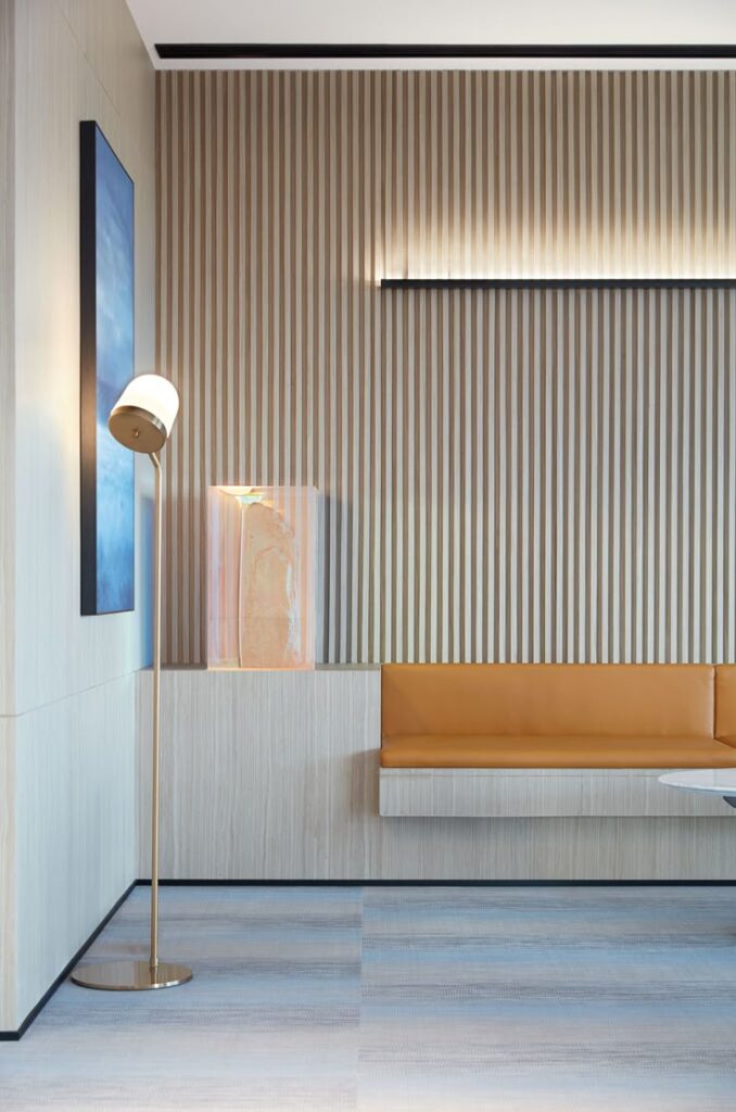 Modern lobby interior with striped wall panels, floor lamp, orange bench seating, and a blue artwork.