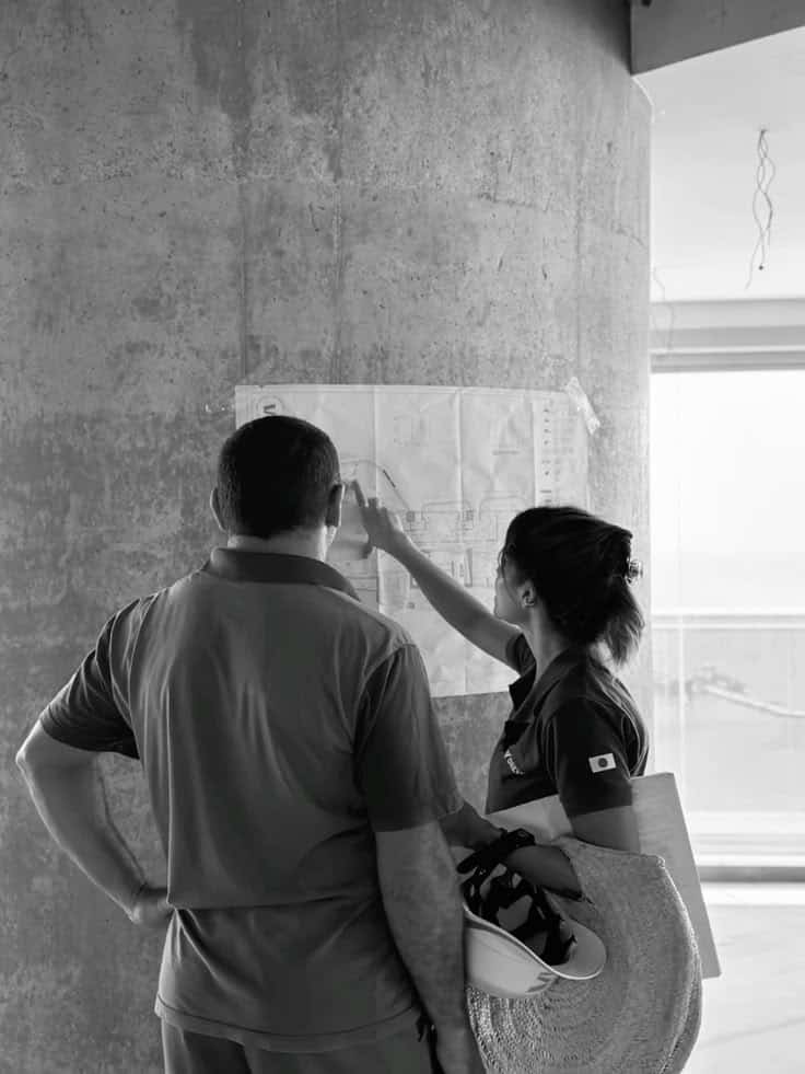 Two people discussing architectural blueprints on a concrete wall at a construction site.