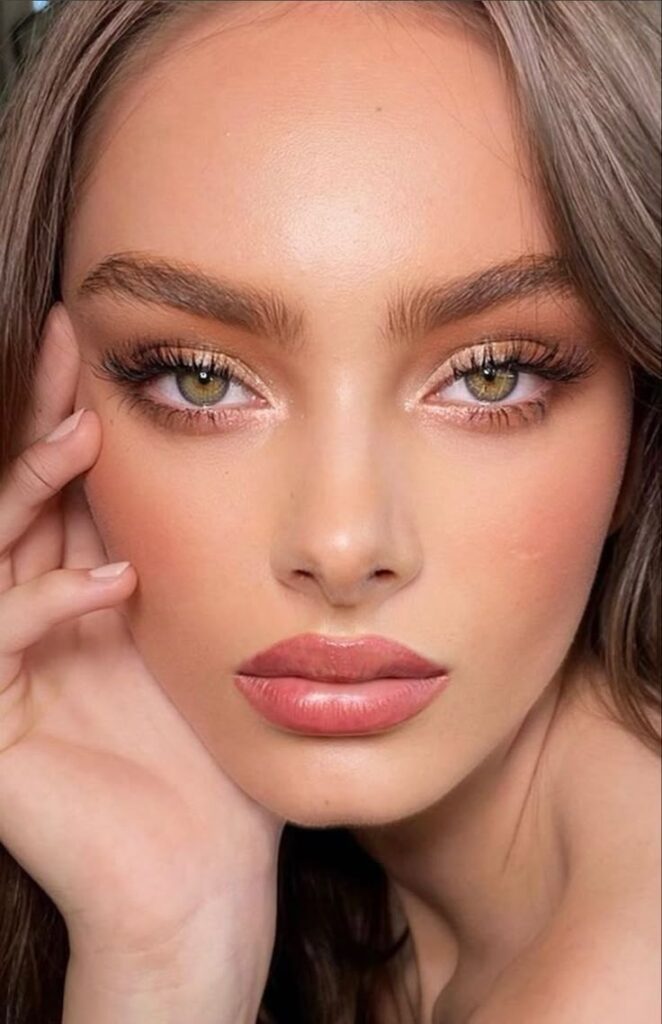 Close-up of a woman with flawless makeup, highlighting bold brows and glossy lips.