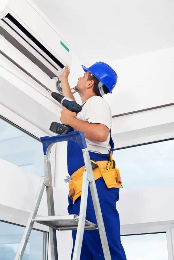 _ 2 Technician in blue overalls installs air conditioner on ladder, holding drill. HVAC maintenance in modern home. | Sky Rye Design Technician in blue overalls installs air conditioner on ladder, holding drill. HVAC maintenance in modern home.