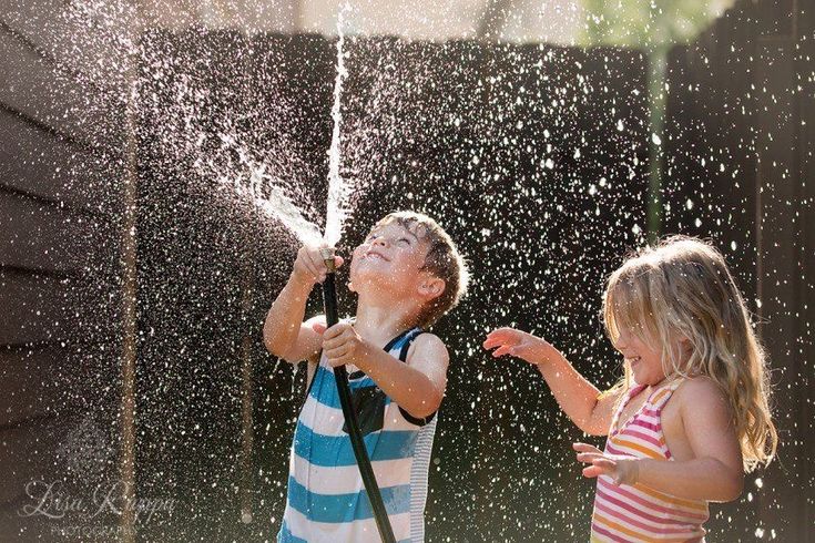 Children joyfully playing with water hose in summer sunlight.