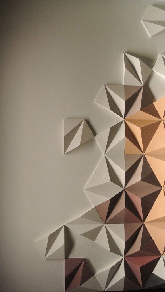 Geometric 3D wall art with triangular patterns in neutral and warm tones on a light background.