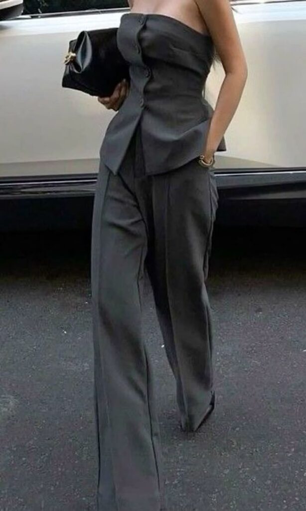 Elegant woman in a stylish gray strapless top and pants, holding a black clutch. Fashionable street style look.