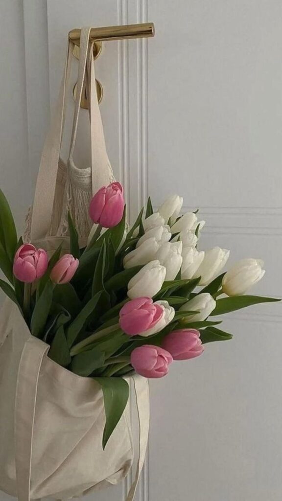 Pink and white tulips in a beige tote bag hanging on a door handle for a stylish home decor touch.
