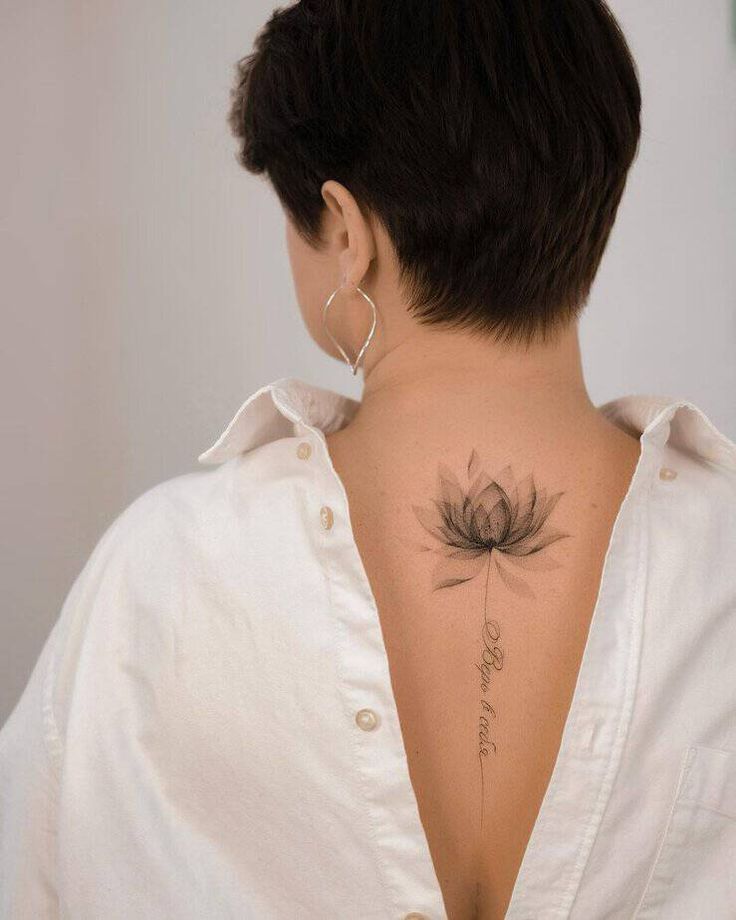 Short-haired person with lotus tattoo on back, white shirt open at back, silver hoop earrings.