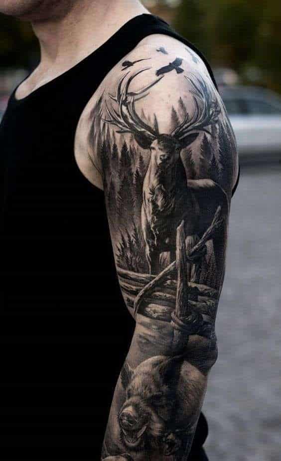 Detailed forest and wildlife tattoo sleeve featuring a stag and bear on a man's arm in a black tank top.