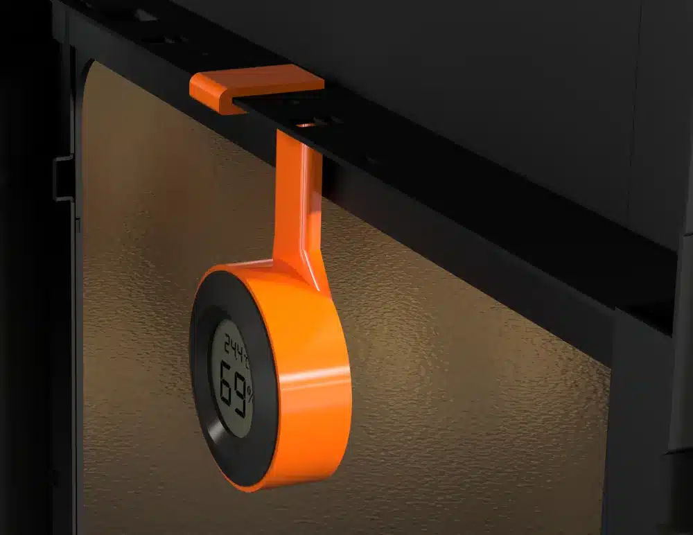 Orange digital humidity and temperature sensor with percentage display, mounted on a metal surface.