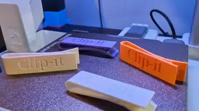 3D printer creating colorful Clip-it clips on a textured platform.