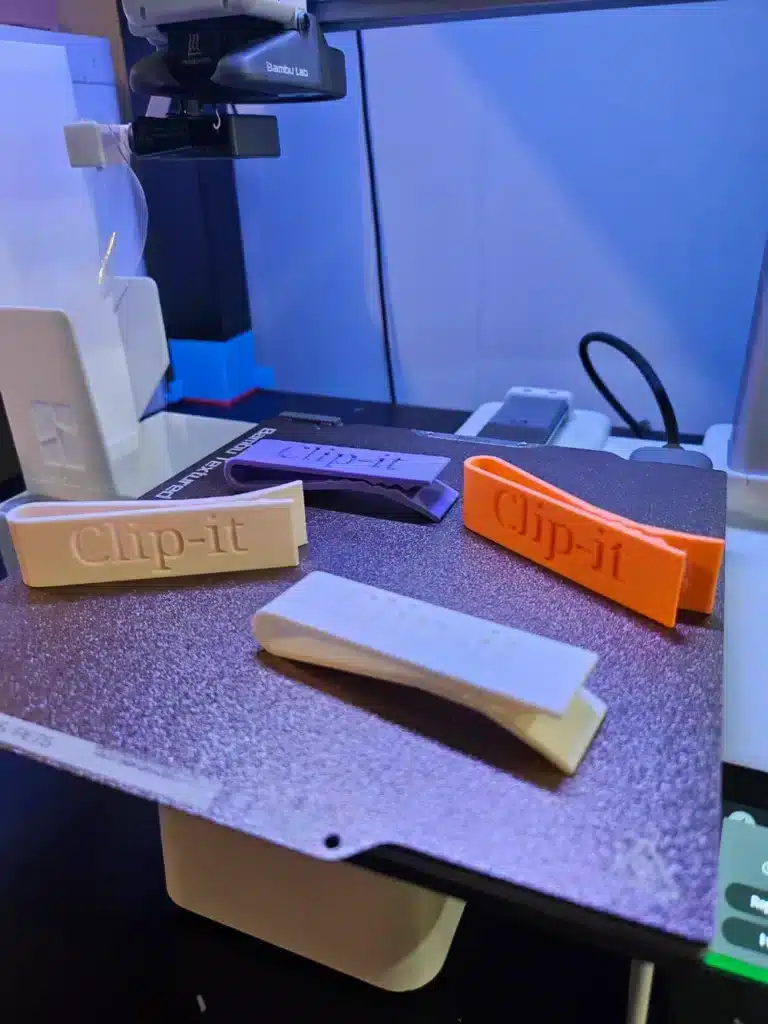 3D printer creating colorful Clip-it clips on a build plate, showcasing various stages of completion.