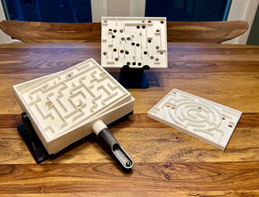 White plastic maze puzzles with various designs on a wooden table, showcasing intricate paths and holes.