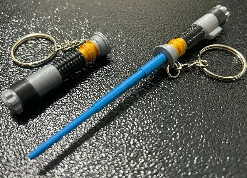 Miniature lightsaber keychains on a textured black surface.