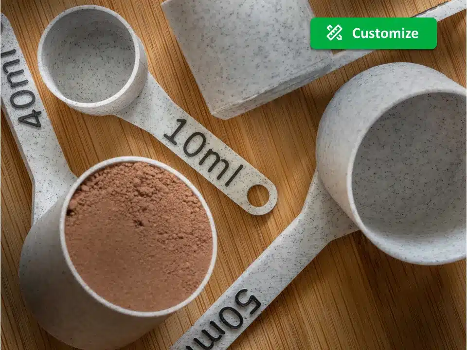 Set of speckled measuring cups on wooden surface, featuring 10ml, 40ml, and 50ml sizes, one filled with cocoa powder.