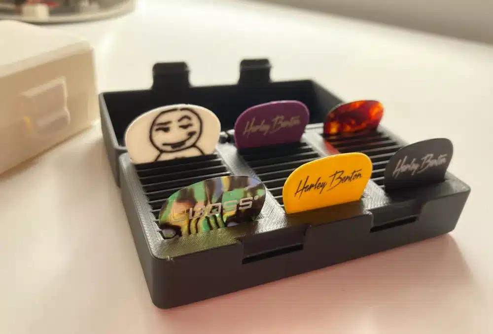 Guitar picks in various colors and designs organized in a black holder on a white surface.