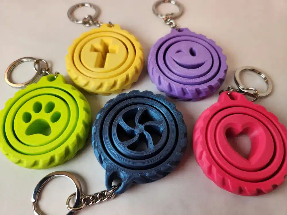 Colorful 3D-printed tire-shaped keychains with various symbols: paw, cross, smiling face, heart, and propeller.