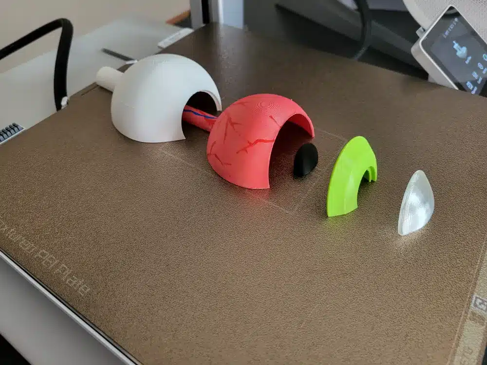 3D printed semi-spherical parts in various colors on a printer bed, showcasing design and fabrication process.