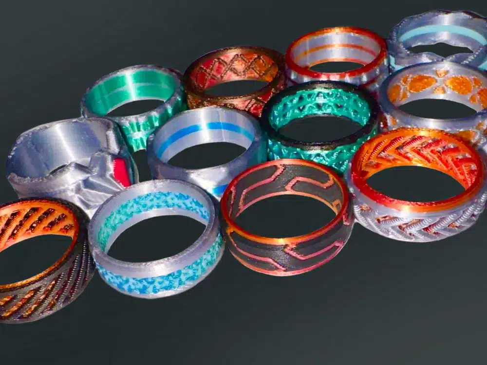 Colorful decorative metal rings with intricate designs displayed on a dark background.