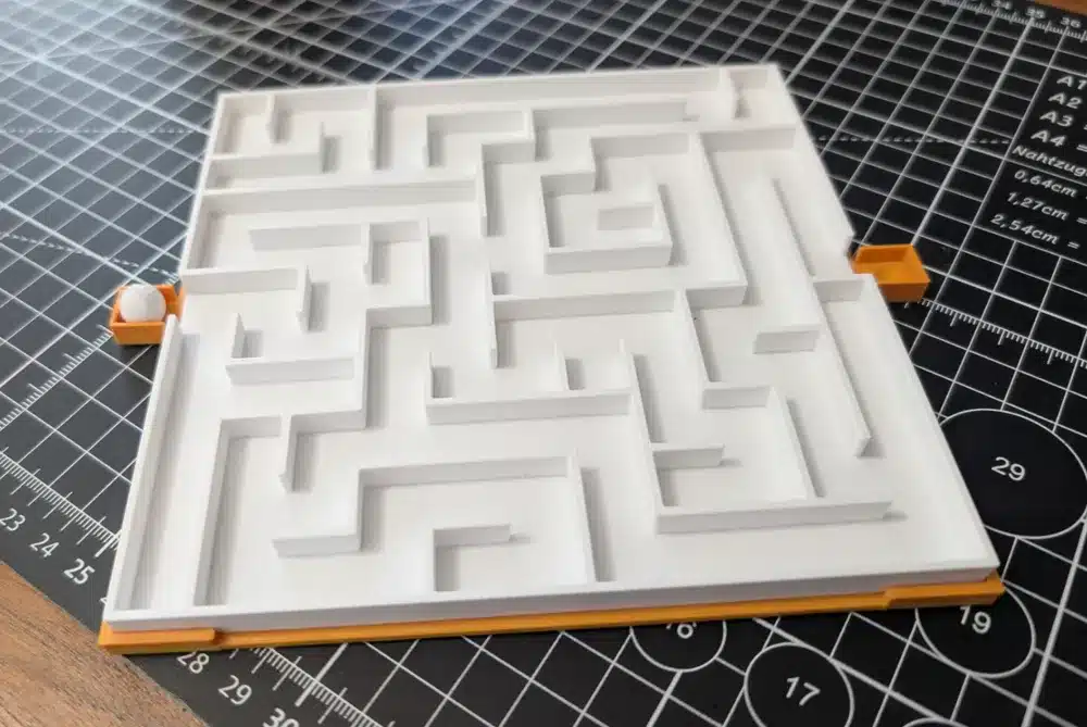 3D printed maze puzzle on a cutting mat with measurement grid, featuring a small ball game.
