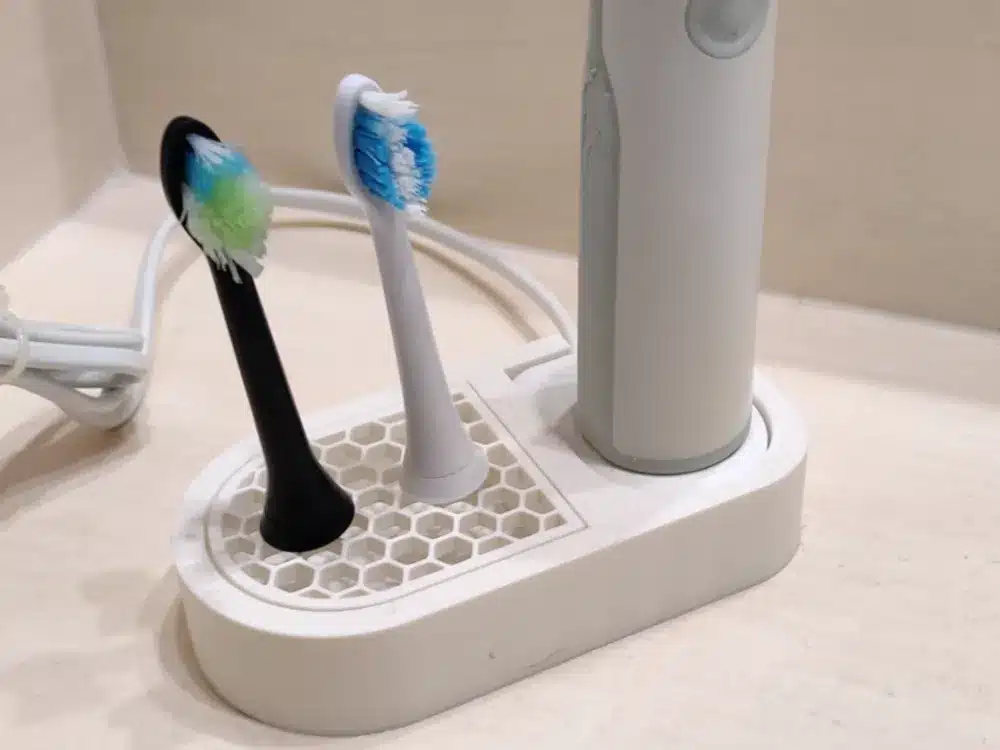 Electric toothbrush with two replacement heads on a white charging stand in a bathroom setting.